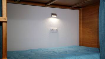 Habitación pequeña con una cama individual, una lámpara en la pared y un enchufe.