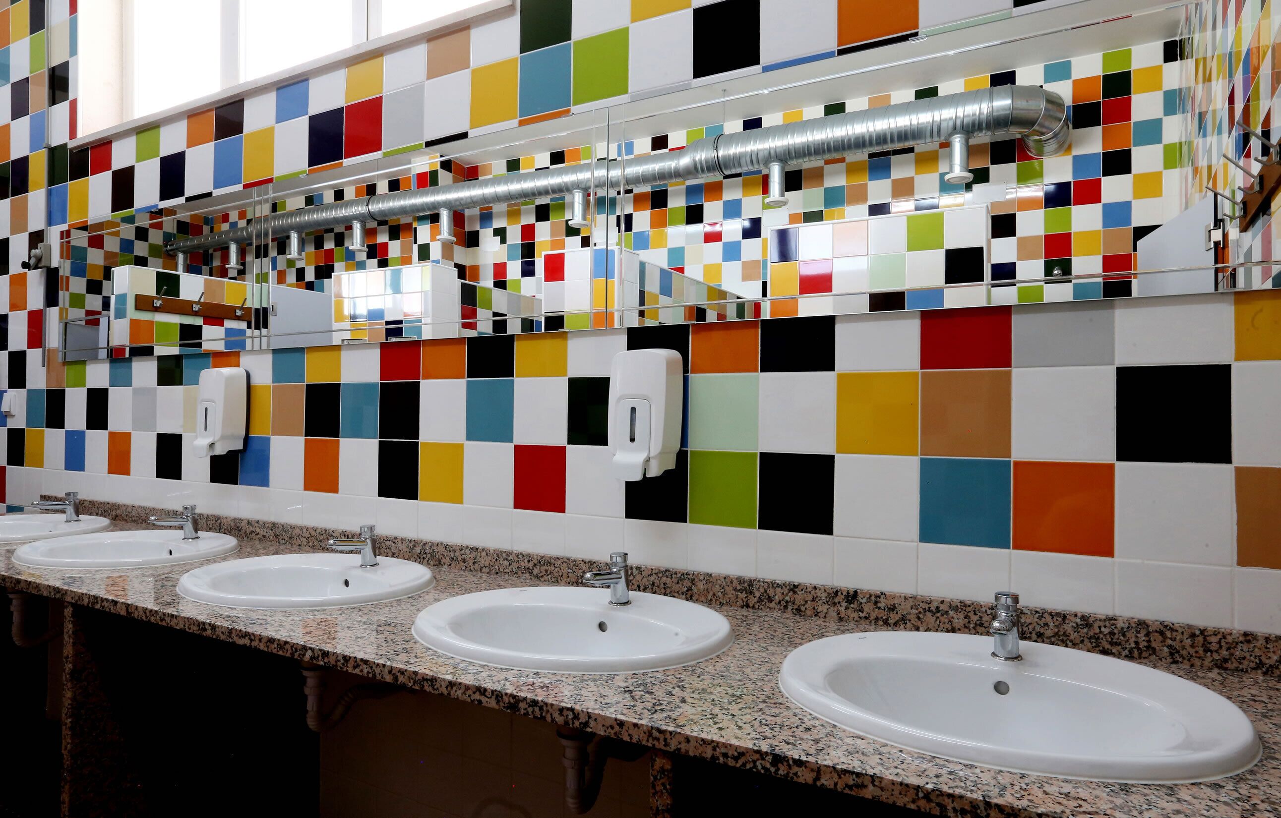 Ein Badezimmer mit vier Waschbecken, einer farbenfrohen Fliesenwand und einer Belüftungsanlage.