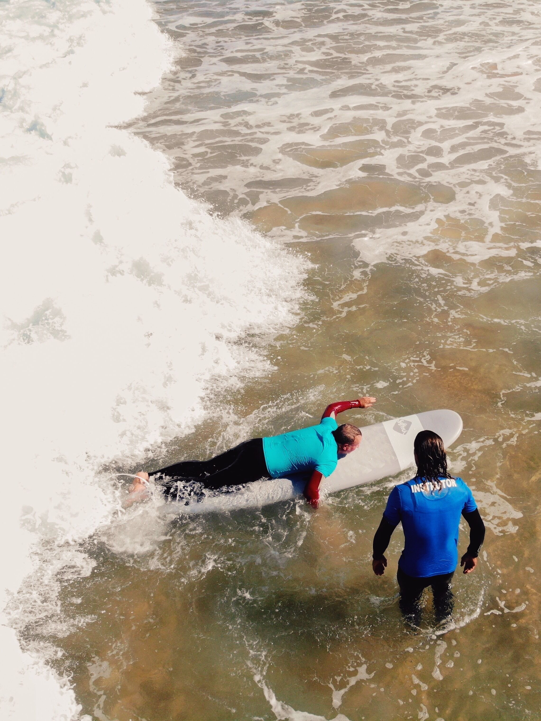 A lifeguard assisting a surfer on a surfboard in the water.