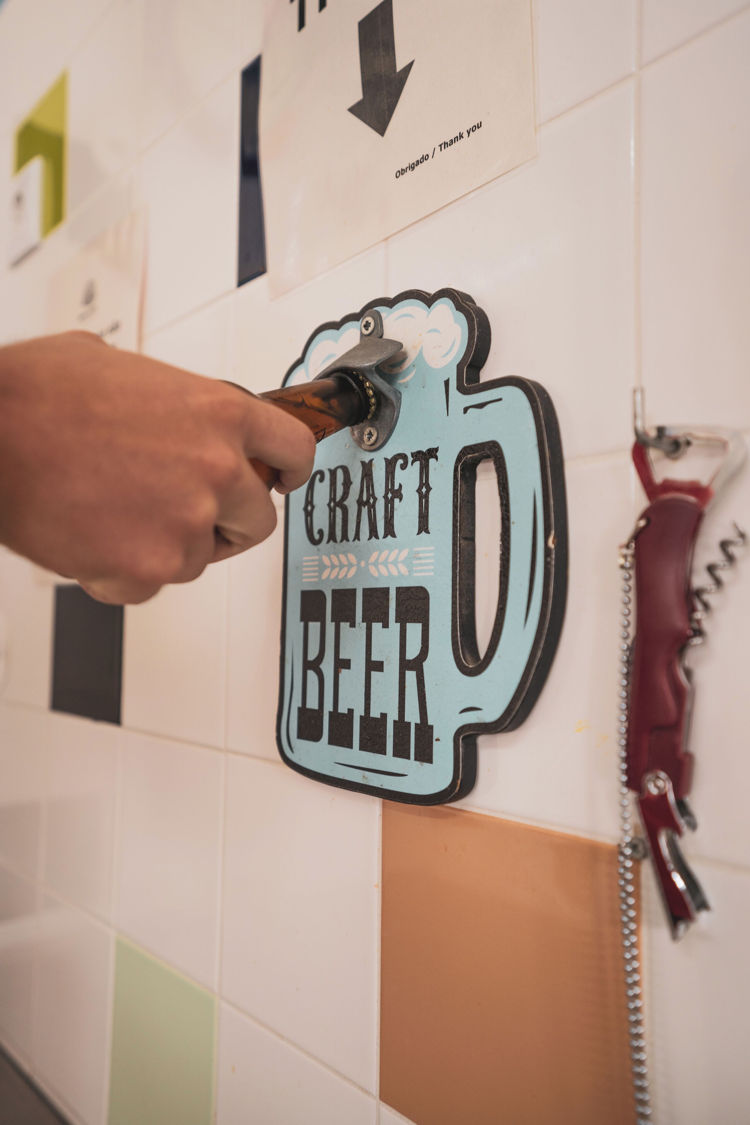 Une main tenant un décapsuleur contre un mur sur lequel est affiché un panneau indiquant « BIÈRE ARTISANALE ».