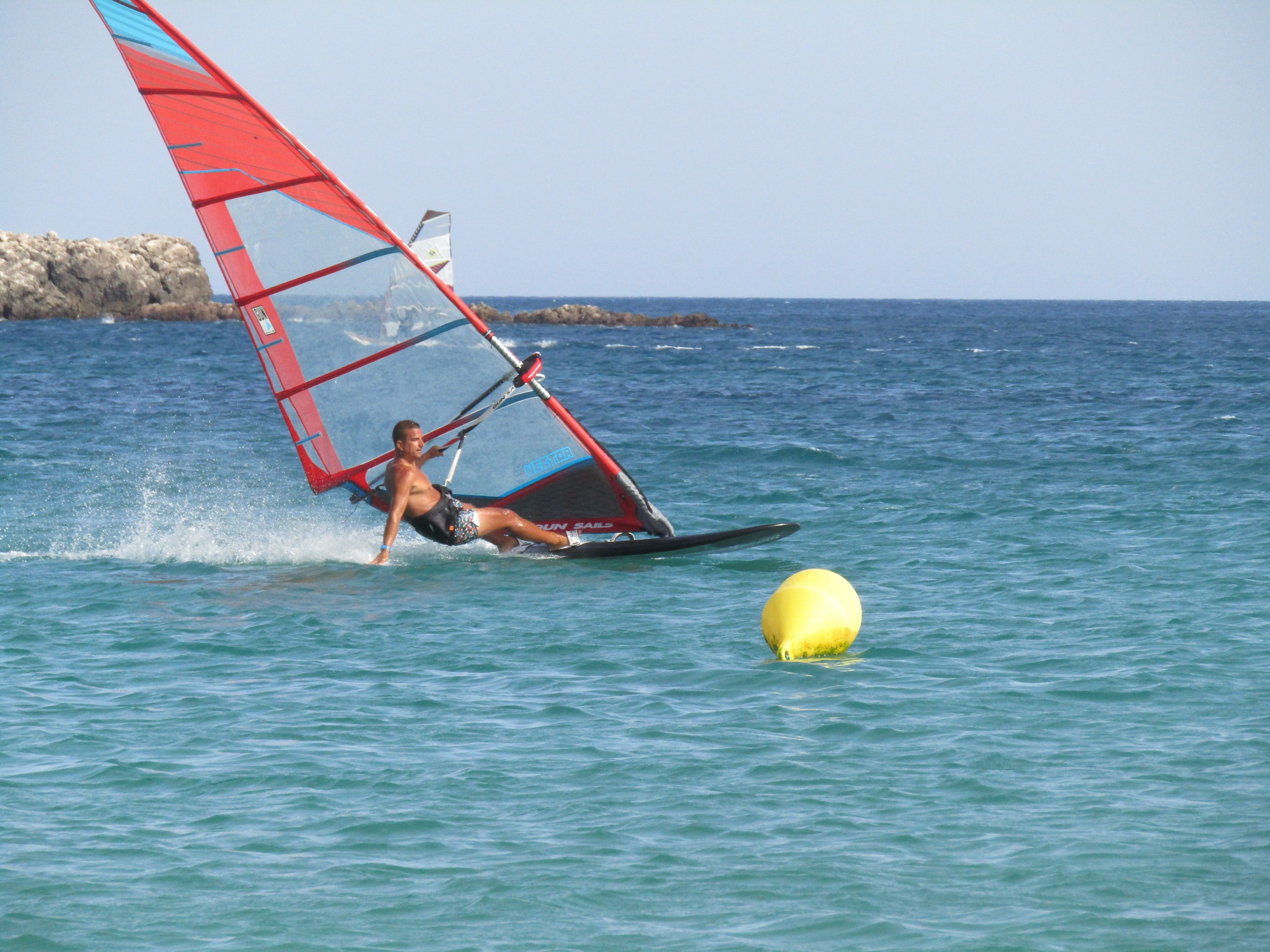 Eine Person windsurft auf ruhiger See mit einem roten Segel.