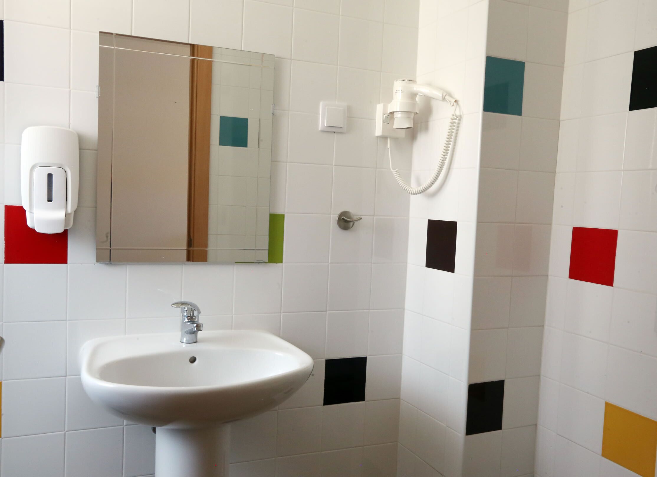 A bathroom with a white sink, a mirror, a hairdryer, and a telephone.
