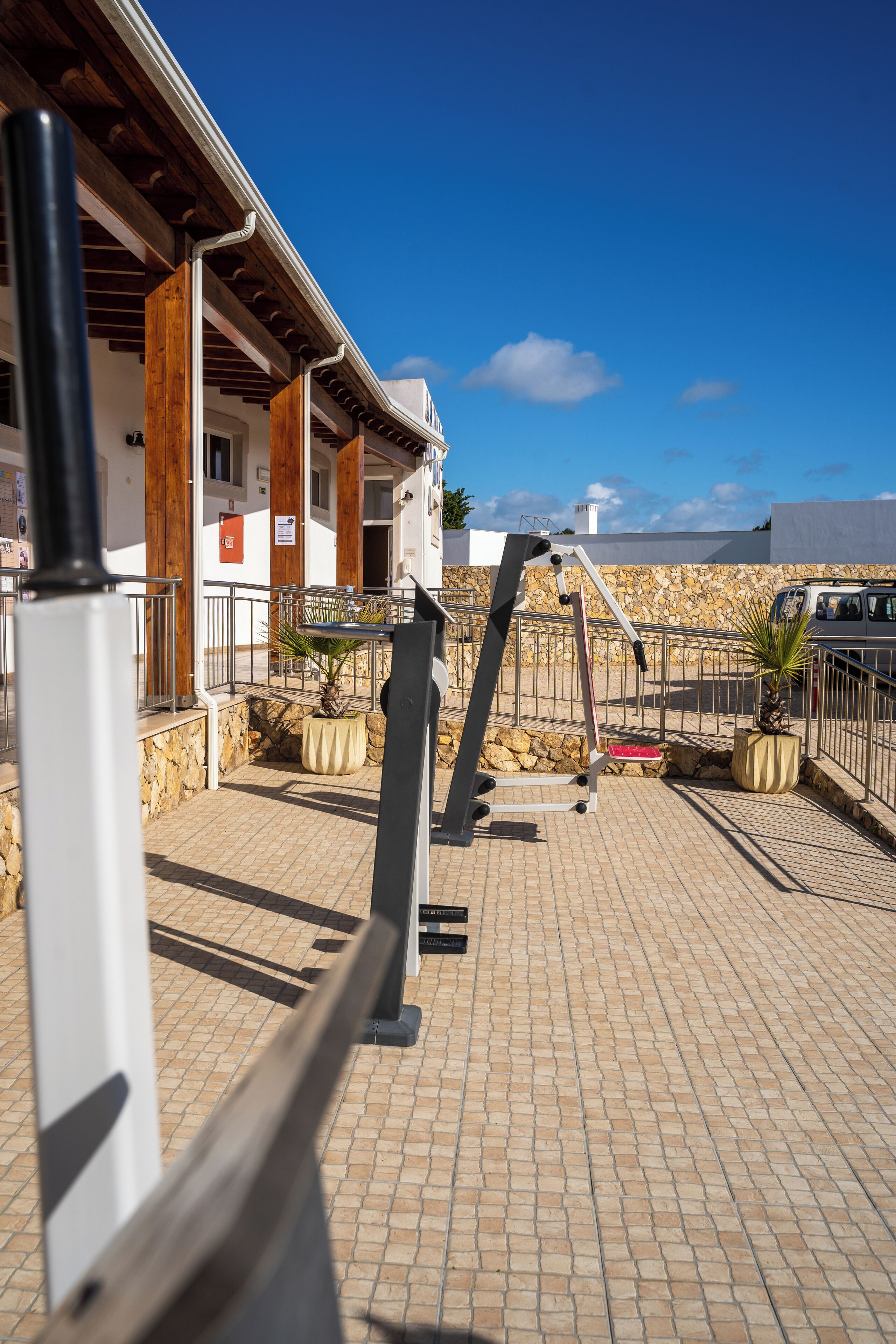 Un espace extérieur aménagé avec une surface pavée, des appareils de musculation, un mur en pierre et un bâtiment avec des poutres en bois.