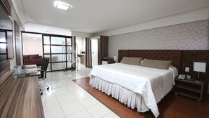 A modern hotel room with a large bed, a desk, and a chair. There is a sliding door leading to a balcony.