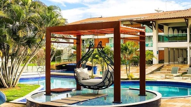 A circular pool with a swing chair, surrounded by a tiled patio and palm trees.