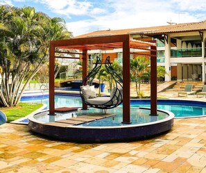 A circular pool with a swing chair, surrounded by a tiled patio and palm trees.