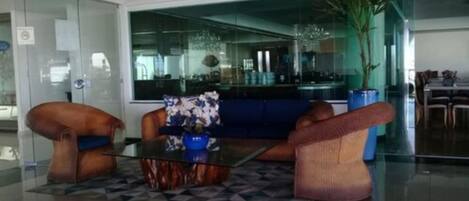 A modern lobby with a glass partition, a sofa, a coffee table, and a dining area visible through the glass.