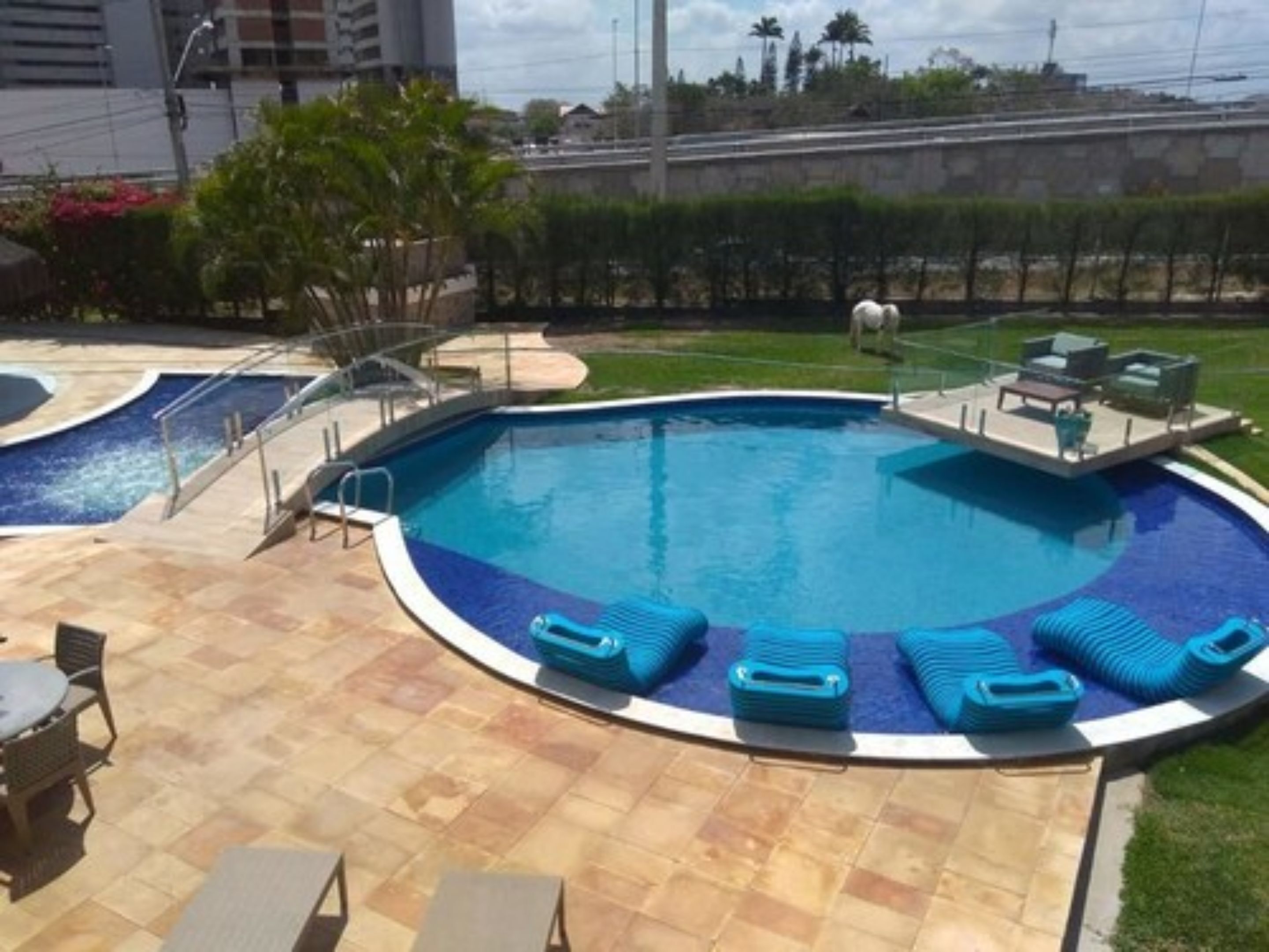 A swimming pool with a curved edge, surrounded by lounge chairs and a small patio area with outdoor furniture.