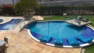 A swimming pool with a curved edge, surrounded by lounge chairs and a small patio area with outdoor furniture.