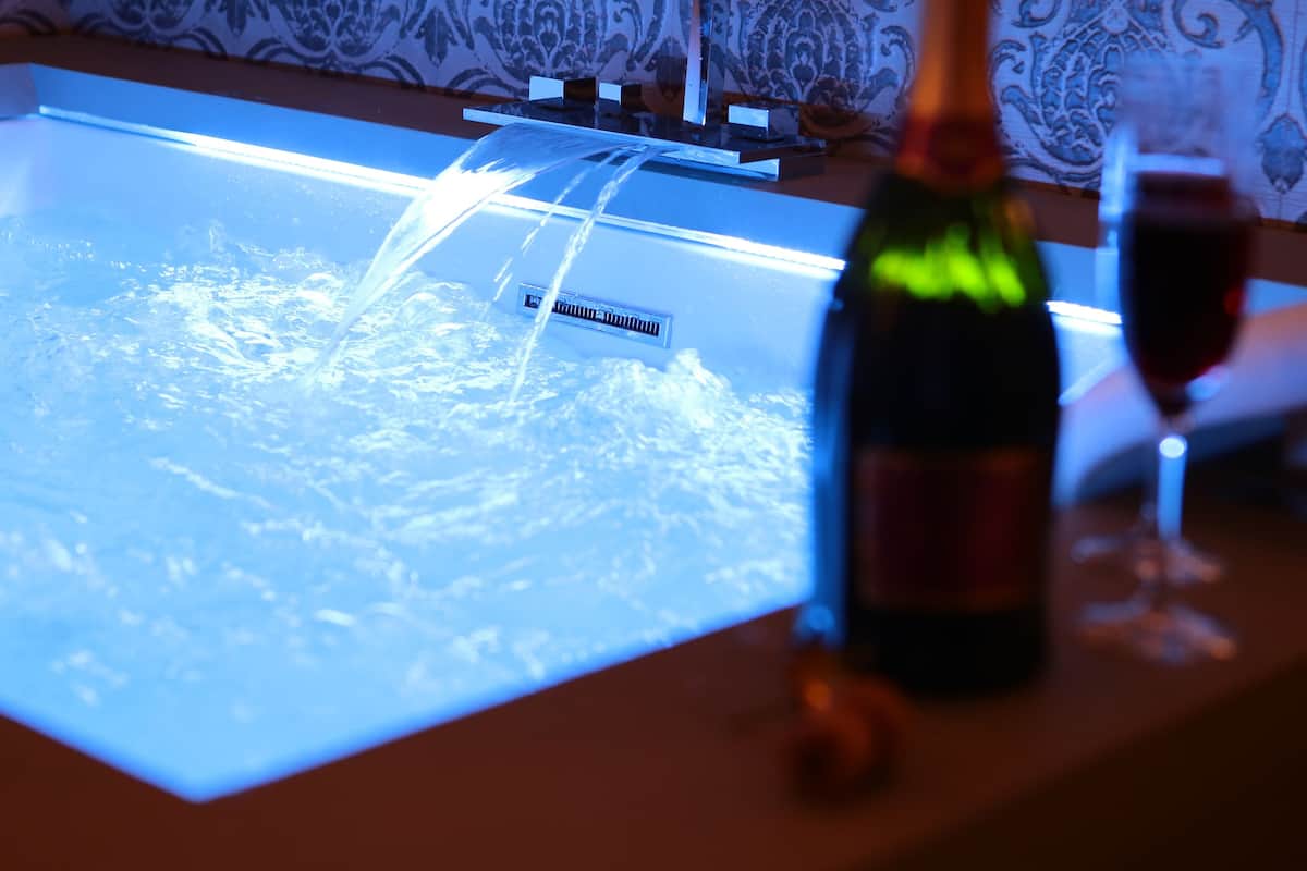 Une baignoire remplie d’eau, une bouteille de champagne et un verre de vin posés sur un comptoir.