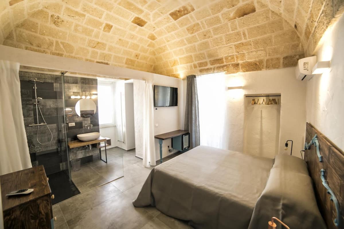 Une chambre avec un plafond en pierre, un grand lit, une table de chevet, une télévision et un espace douche.