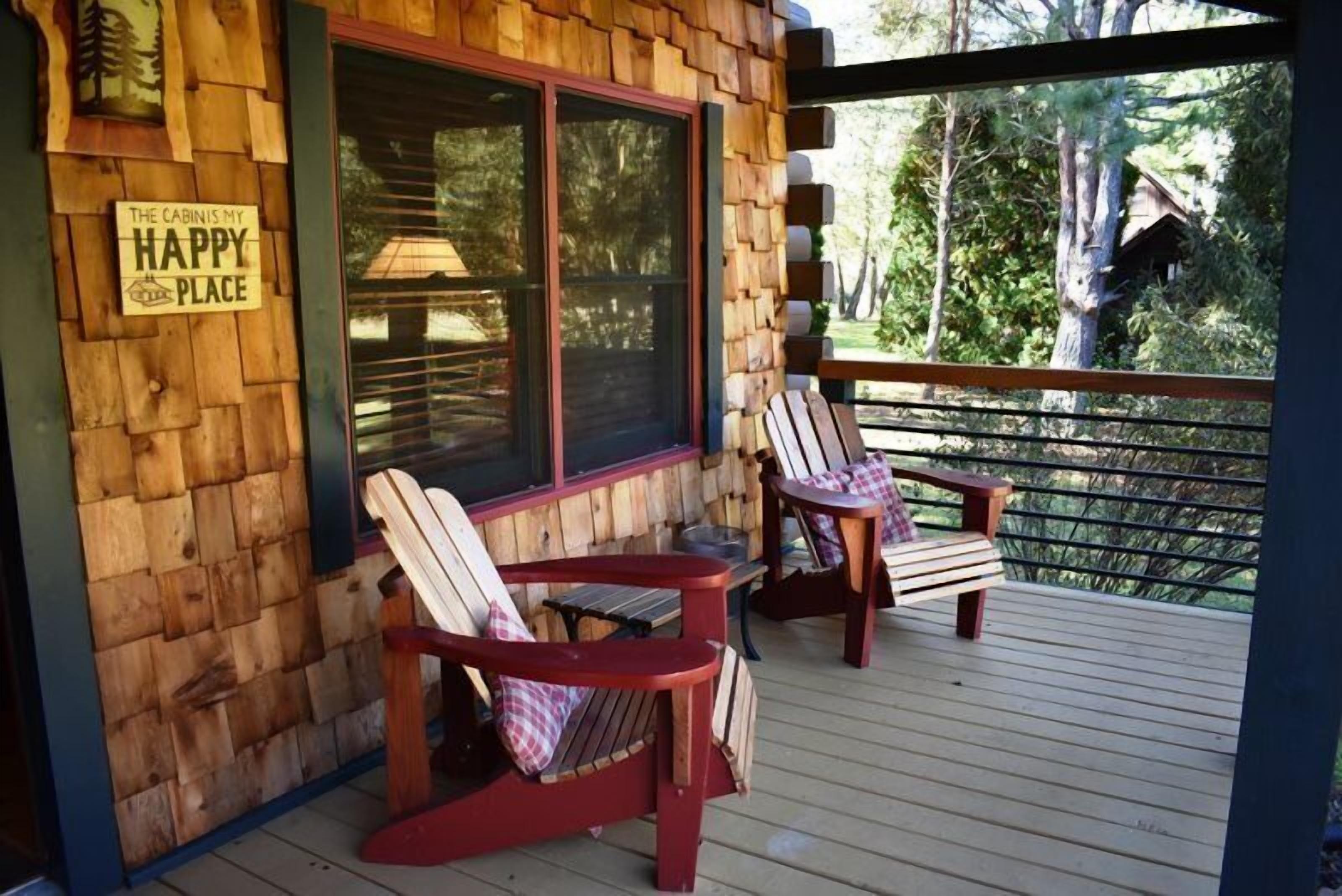 A wooden cabin with a deck, two Adirondack chairs, and a sign that reads "The Cabin is My Happy Place."