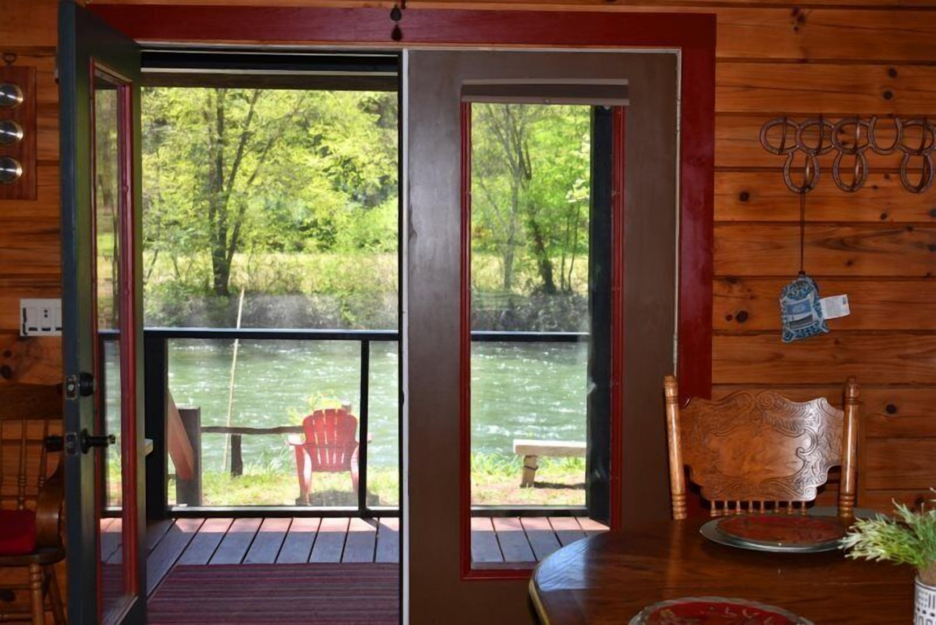 A wooden cabin with a deck overlooking a river, a red chair, and a bench.