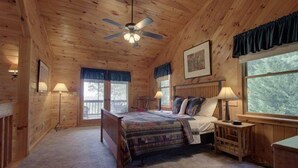 Ein Schlafzimmer in einer Holzhütte mit einem Bett, zwei Nachttischen, einem Deckenventilator und großen Fenstern.