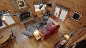 Ein gemütliches Blockhaushaus-Interieur mit Kamin aus Stein, Holzwänden, einer Essecke und einem Wohnzimmer mit rotem Sofa und Lampe.