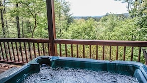 Ein Whirlpool auf einer Holzterrasse mit Blick auf ein bewaldetes Gebiet.