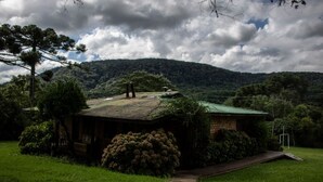 Un chalet rustique avec un toit végétalisé, entouré d’une végétation luxuriante et avec une colline en arrière-plan.