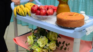 Ein Tisch mit einer Obstschale, die Bananen, Äpfel und eine Karaffe enthält.