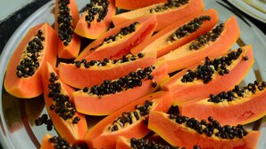 Ein Teller mit Scheiben von Papaya und schwarzen Kernen auf einer spiegelnden Oberfläche.