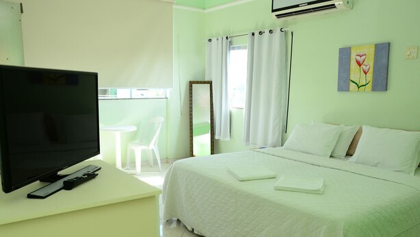 Ein Hotelzimmer mit einem Bett, einem Fernseher auf einem Schreibtisch, einem Sessel und einem Bild an der Wand.