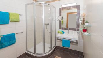 Un baño moderno con cabina de ducha de vidrio, lavamanos con espejo y repisa con artículos de aseo.