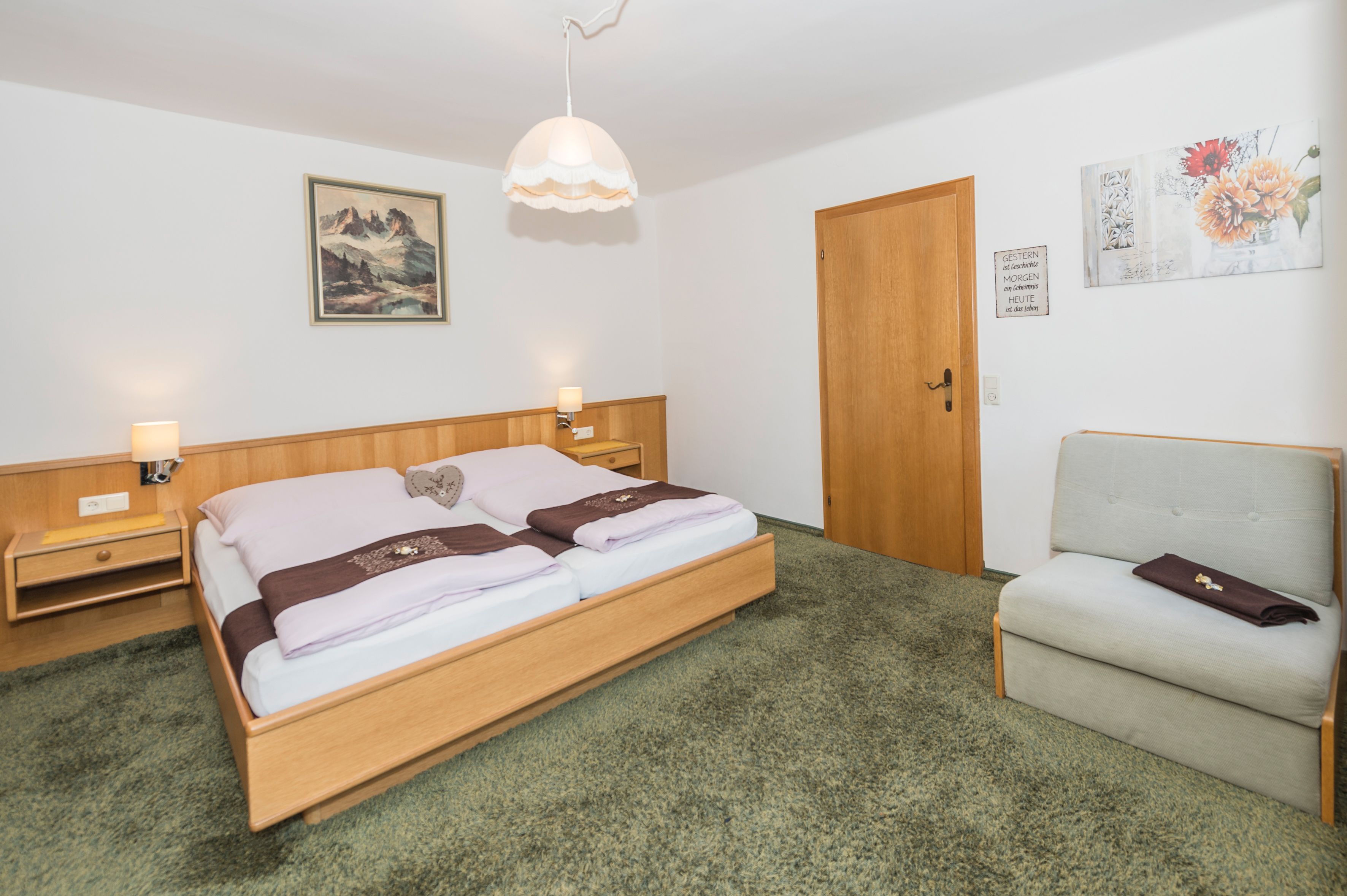 A neatly arranged bedroom with a wooden bed, bedside tables, a chair, and a door.