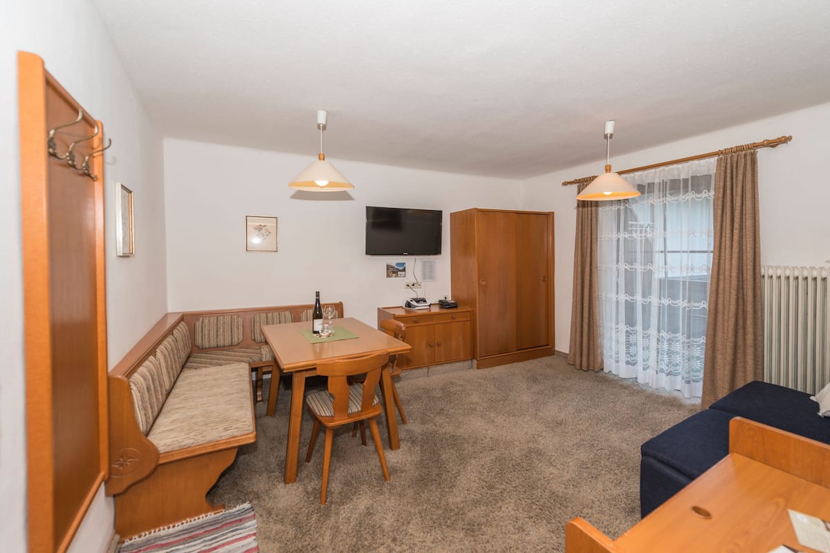 A cozy room with a wooden bench, a dining table, and a TV mounted on the wall.