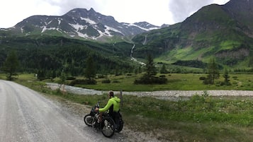 Eine Person im Rollstuhl auf einem Schotterweg, im Hintergrund eine Berglandschaft.