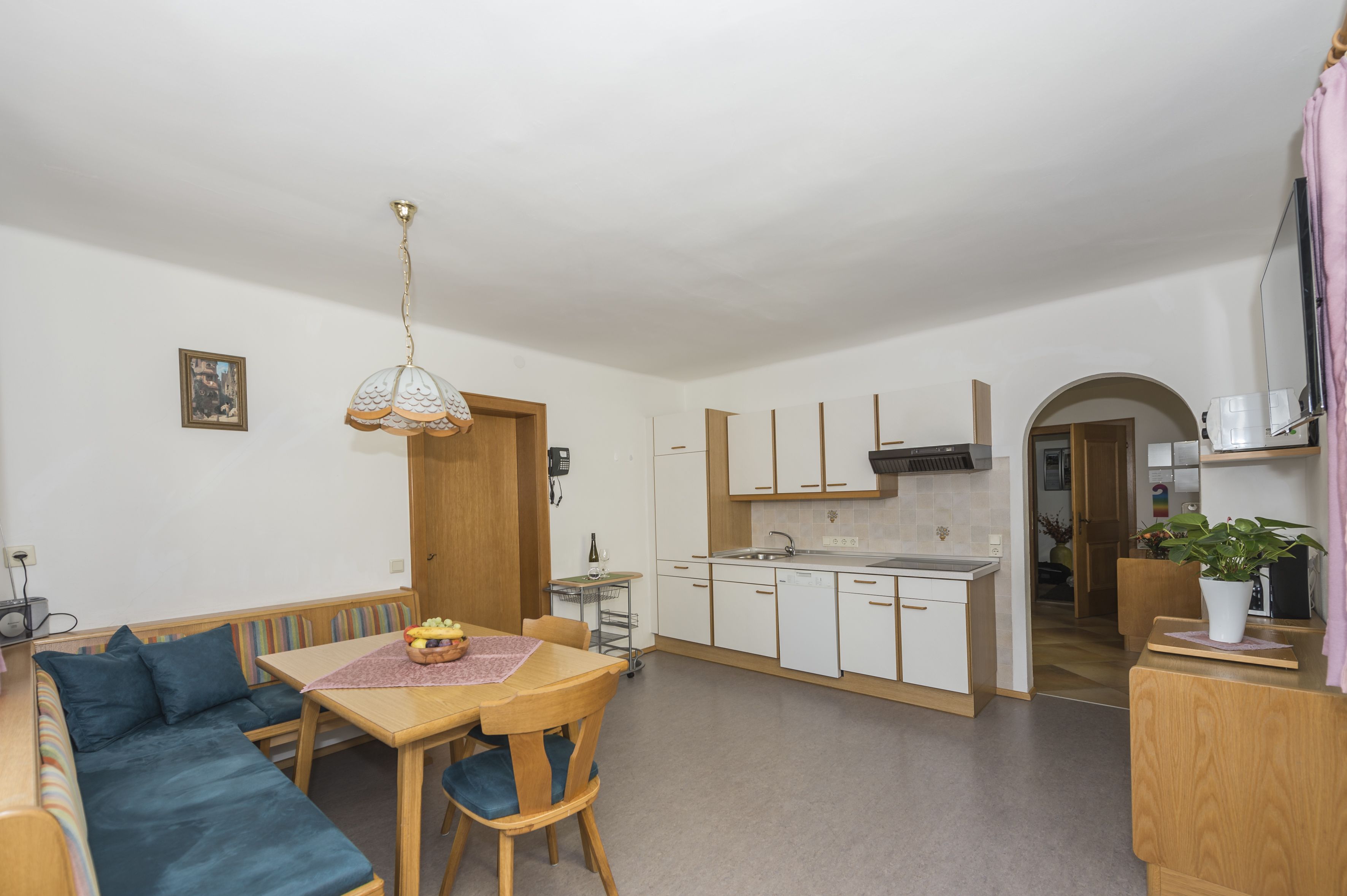 A compact living space with a kitchenette, a dining area with a table and chairs, a sofa, and a ceiling light fixture.