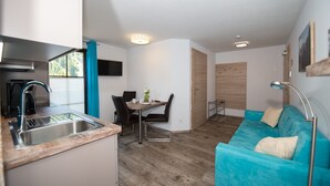 Un espacio habitable compacto con kitchenette, comedor y un sofá color turquesa.