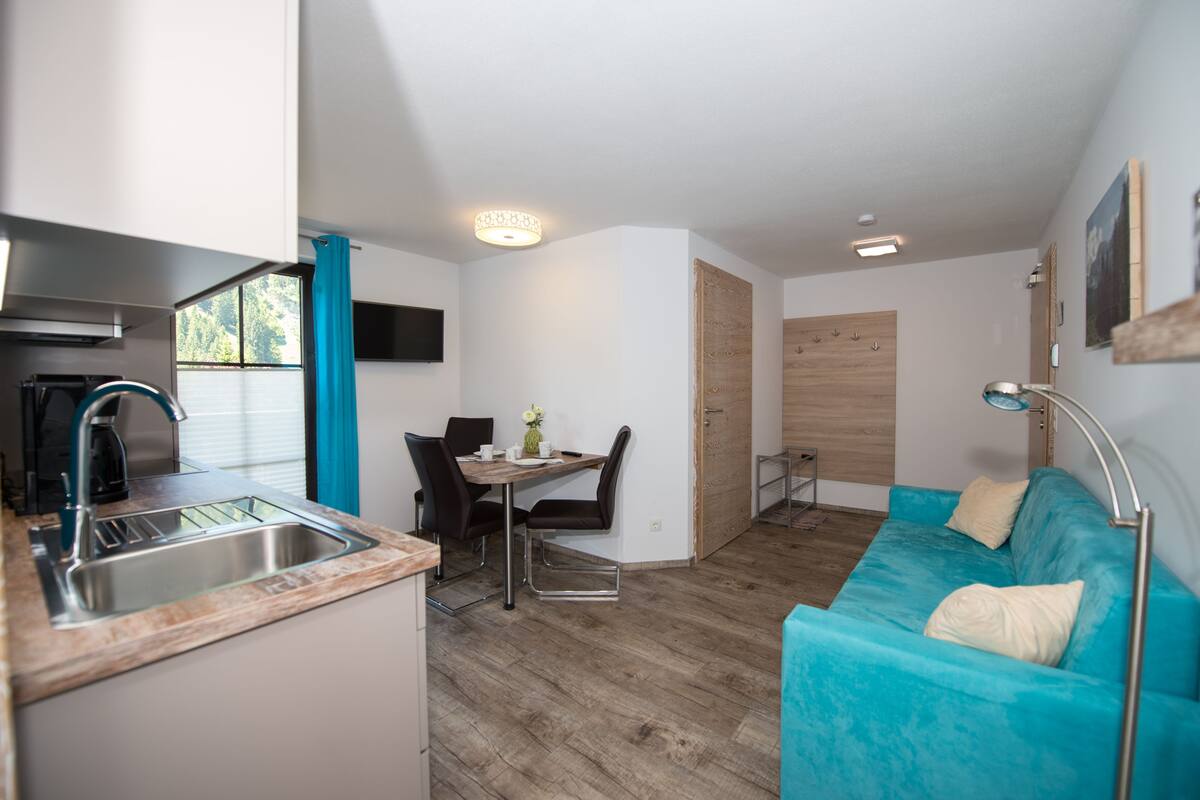 A compact living space with a kitchenette, dining area, and a teal sofa.