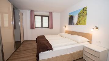 Un dormitorio con una cama, una mesita de noche, una ventana con cortinas, una lámpara de pared y un cuadro.