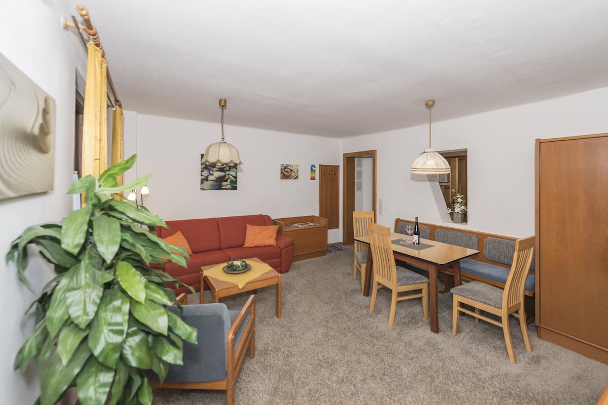 A living room with a sofa, coffee table, dining table, chairs, and a potted plant.