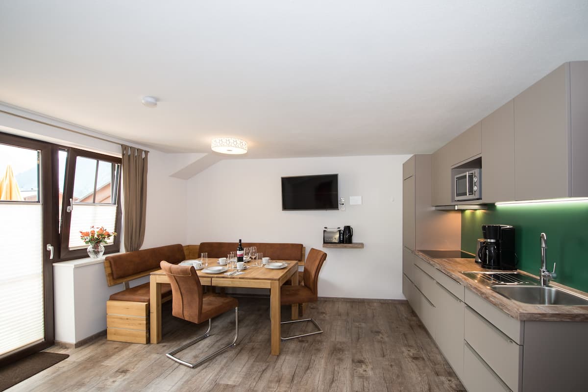 A compact kitchen with a microwave, a coffee maker, and a sink. There is a dining area with a table set for two, and a television mounted on the wall.