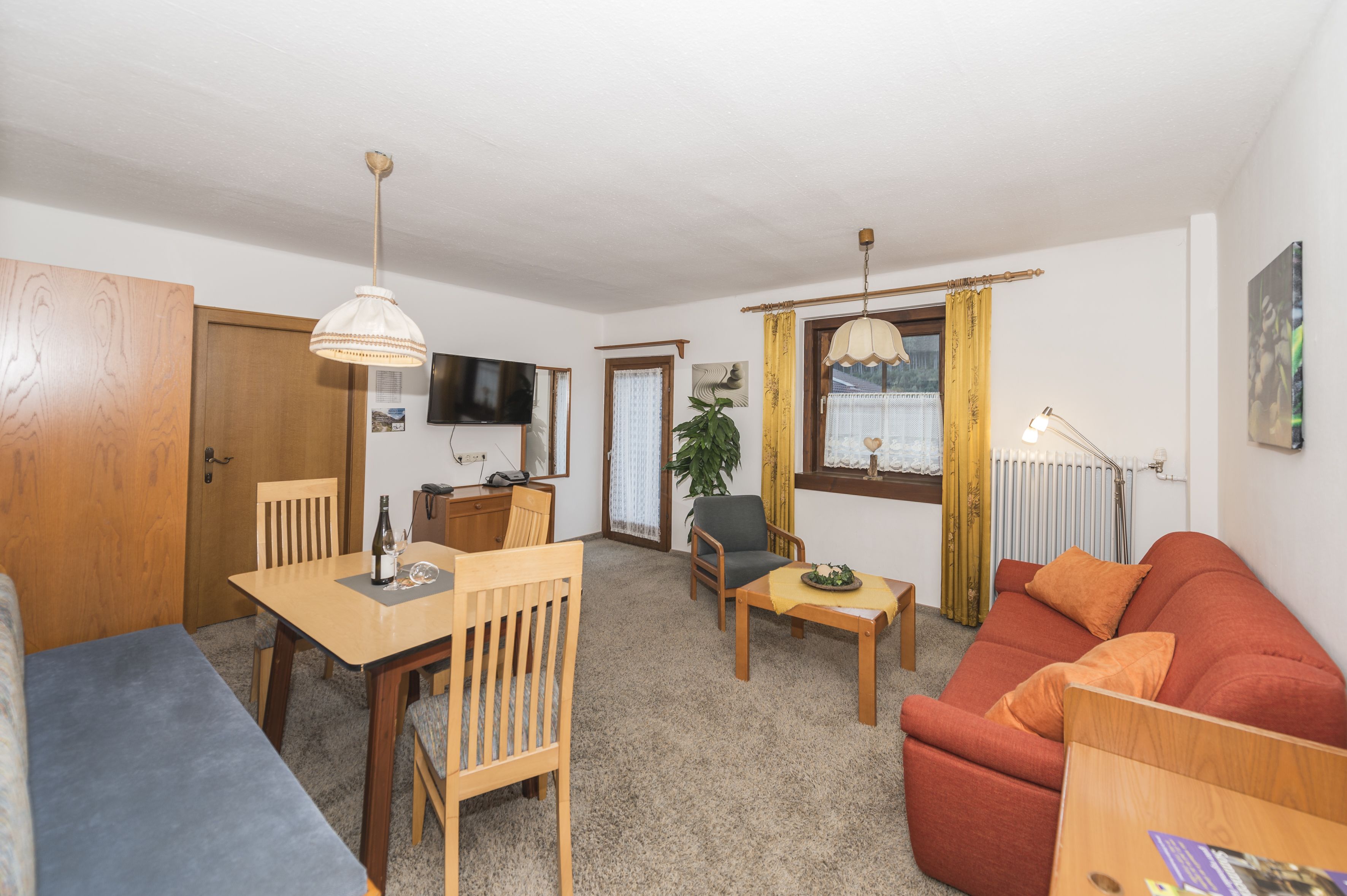 A furnished living room with a wooden dining table, two chairs, a sofa, and a television.