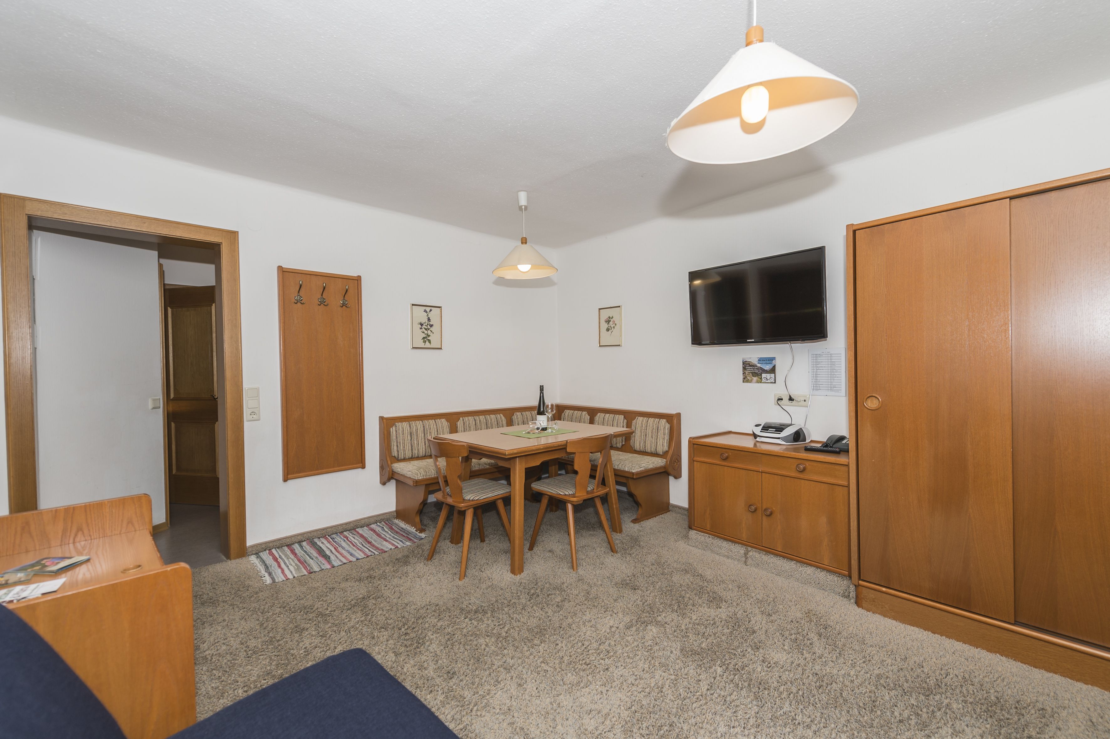 A compact living space with a dining area, a television mounted on the wall, and a wardrobe.