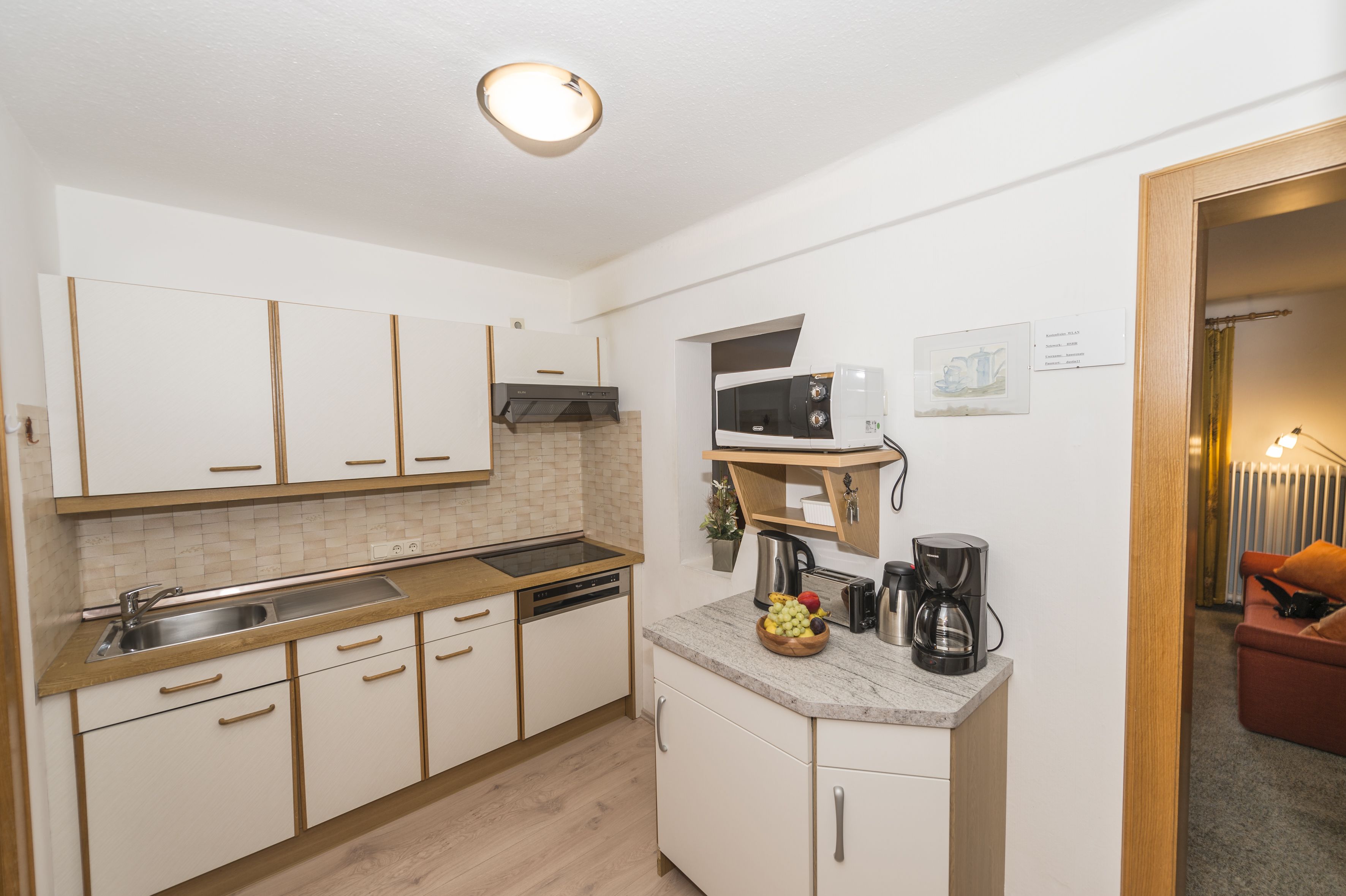 Una cocina compacta con armarios blancos, un microondas, una cafetera y un lavabo.