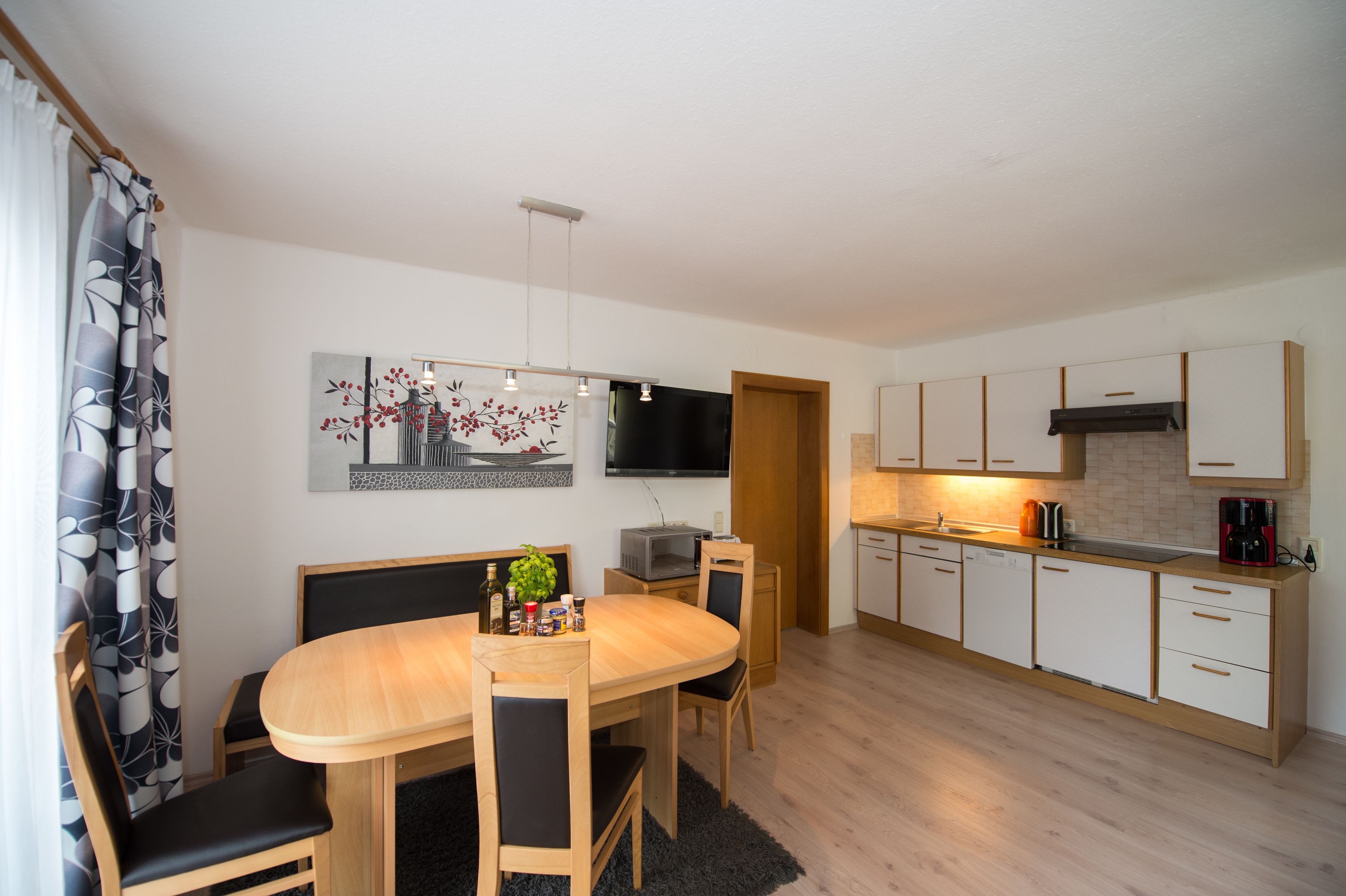 Una cocina moderna con comedor, armarios de madera, televisor de pantalla plana y cafetera.