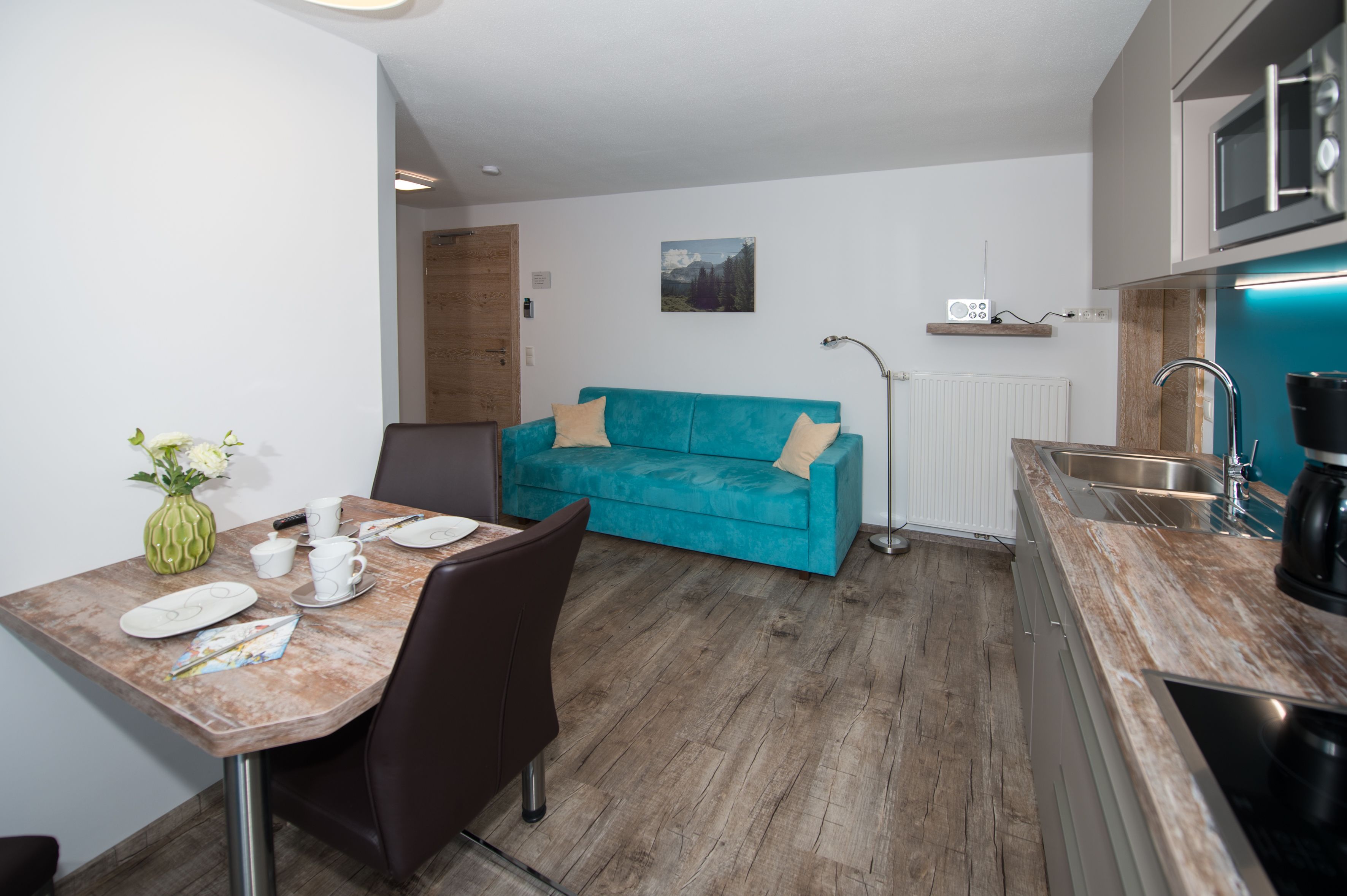 Une cuisine compacte avec un canapé de couleur turquoise, une table à manger avec des chaises et une machine à café.