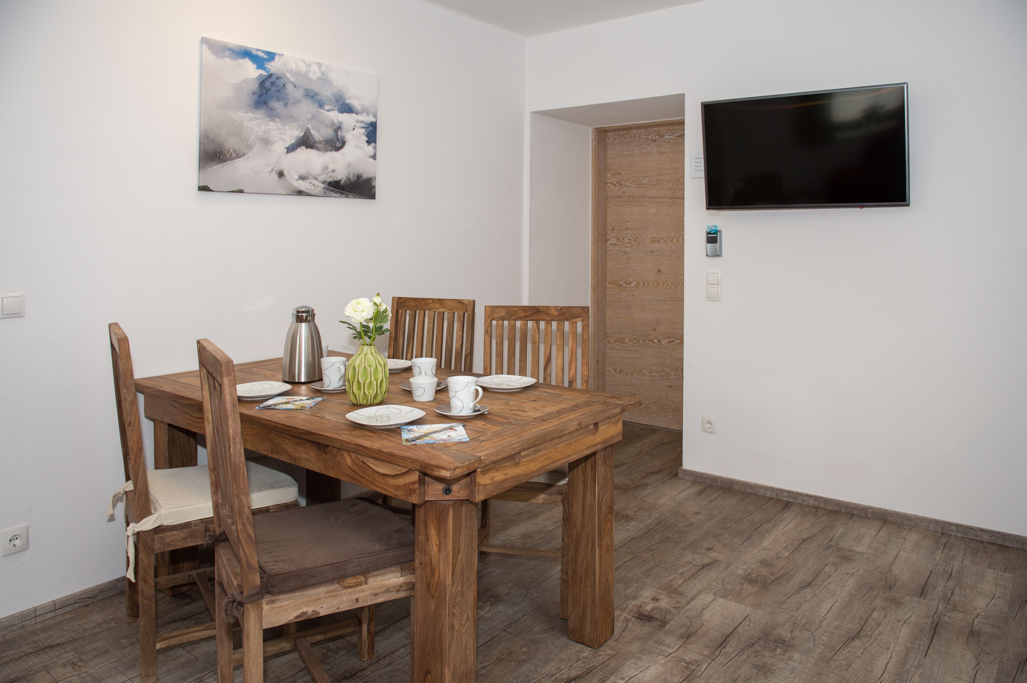 Un comedor con una mesa de madera, sillas, un jarrón con flores y un cuadro en la pared.