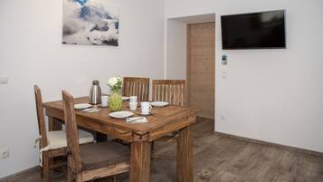 A dining area with a wooden table, chairs, a vase with flowers, and a painting on the wall.