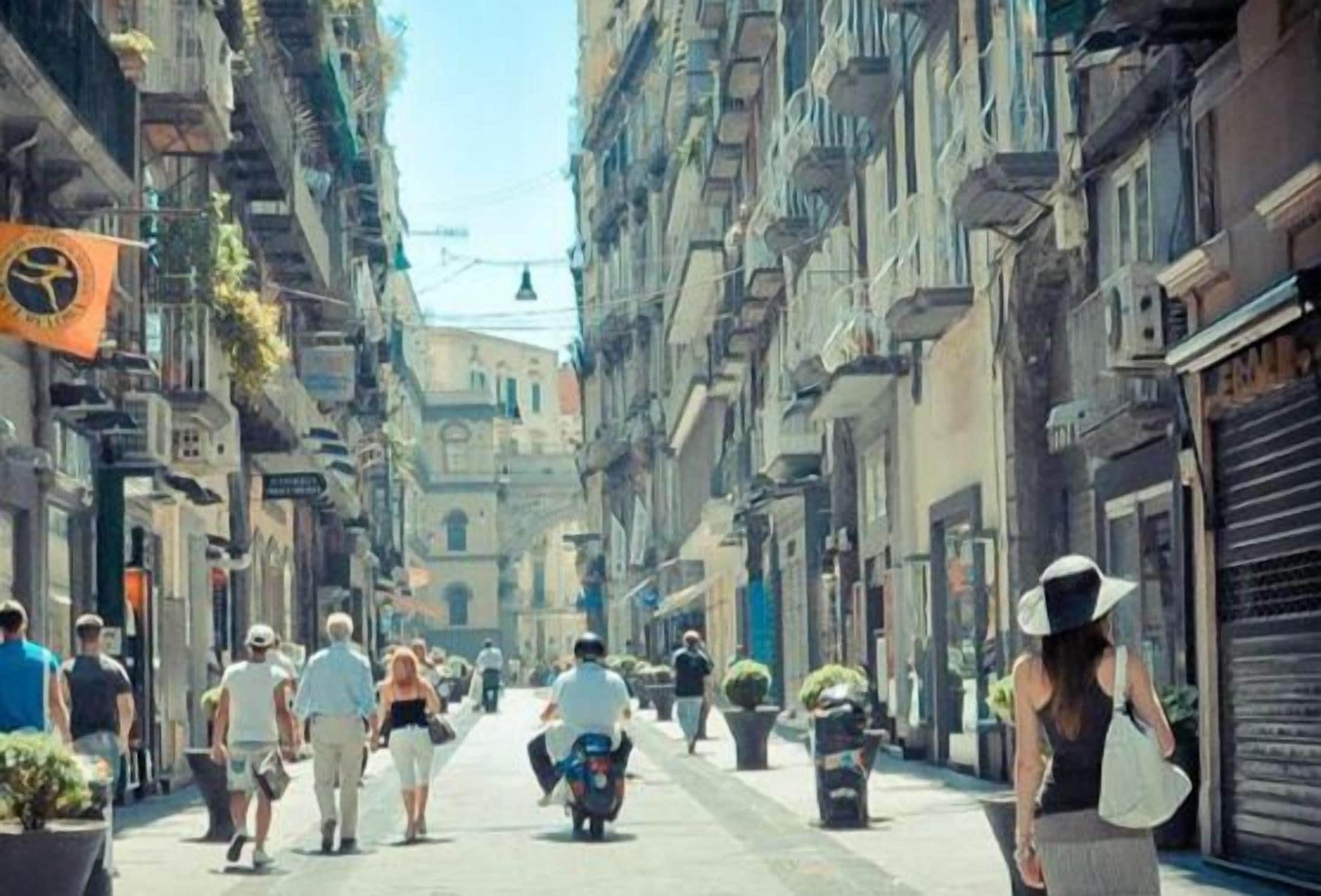 A narrow street lined with multi-story buildings, some with balconies and plants.