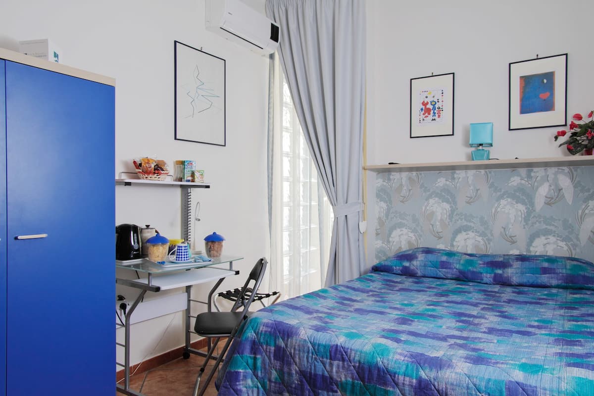 A bedroom with a bed, a desk, a chair, a wardrobe, and a window with curtains.