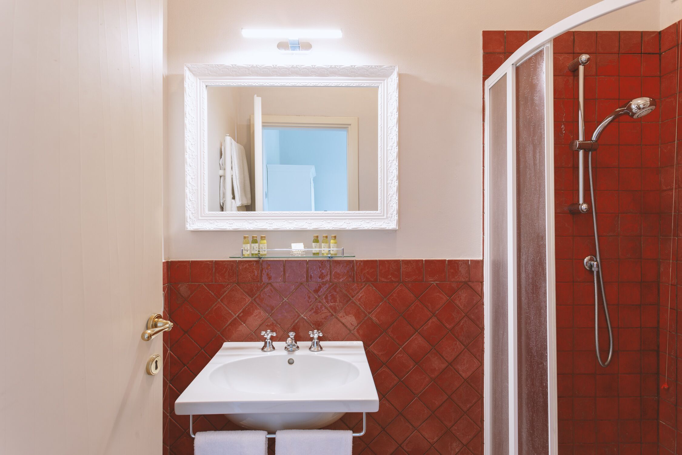 Une salle de bain avec un lavabo blanc, un miroir et un espace douche aux carreaux rouges.
