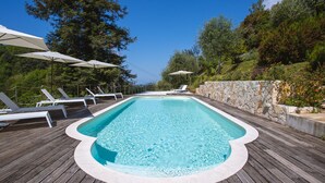 A rectangular swimming pool with a wooden deck, surrounded by lounge chairs and umbrellas. - Villa Borgovecchio B&B (Camaiore)