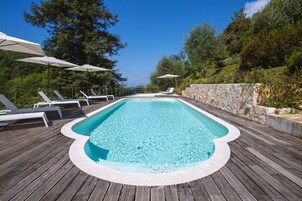 Una piscina rectangular con muelle de madera, rodeada de sillones de playa y sombrillas.