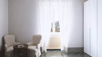 A room with two white chairs, a small round table, a radiator, and a window with sheer curtains.