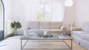 A living room with a beige sofa, a glass coffee table, a floor lamp, and a window with sheer curtains. - Villa Borgovecchio B&B (Camaiore)