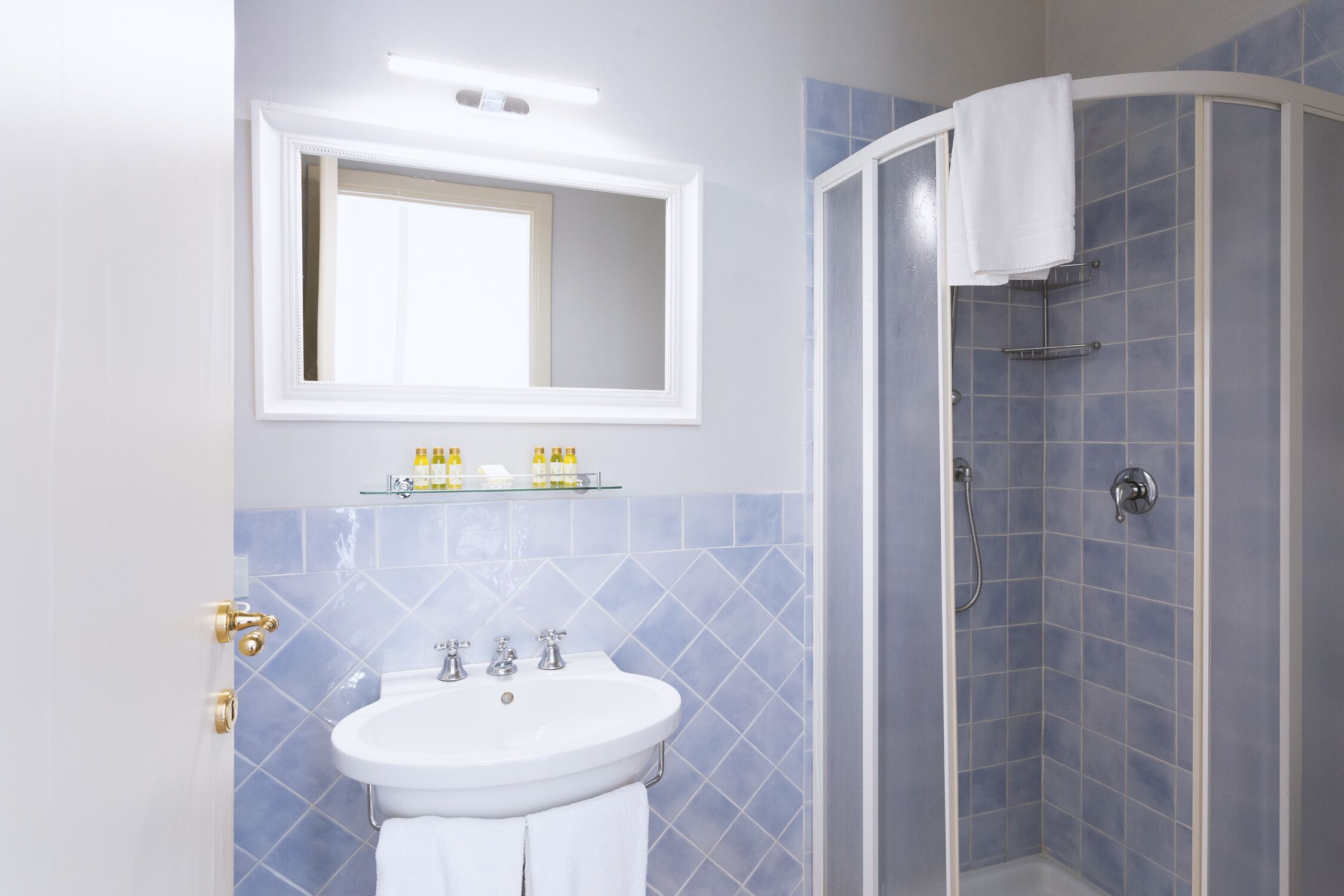 A bathroom with a white sink, a mirror above it, and a shower with a white towel hanging on the door.