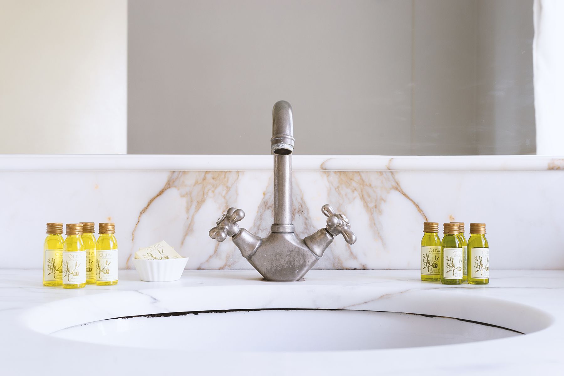 Un lavabo de salle de bain avec un seul robinet, entouré de bouteilles d’huile d’olive.
